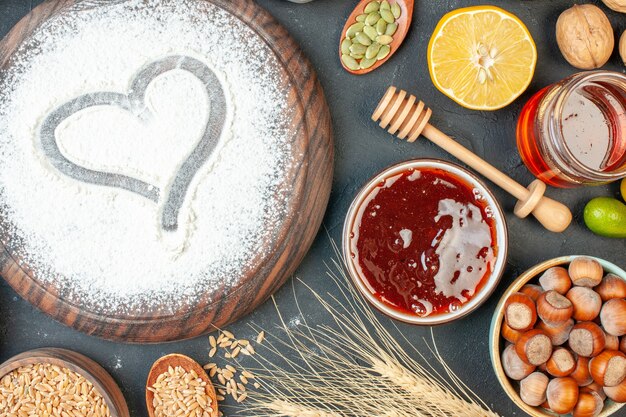 Top view white flour in heart shape with nuts on dark fruit sweet pie tea dessert biscuit cake sugar pastry