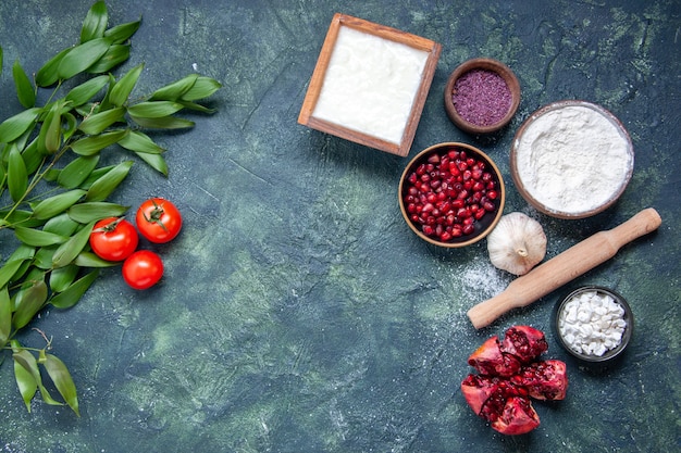 Top view white flour with pomegranates and tomatoes on dark blue background color food dough fruit green