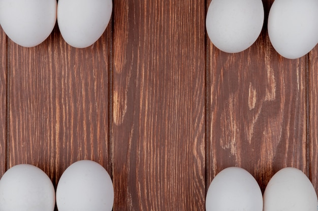 Top view of white fresh chicken eggs arranged in different sides on a wooden background with copy space