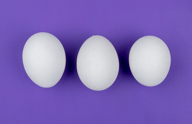 紫色の背景に並んで配置された白い新鮮な鶏の卵のトップビュー