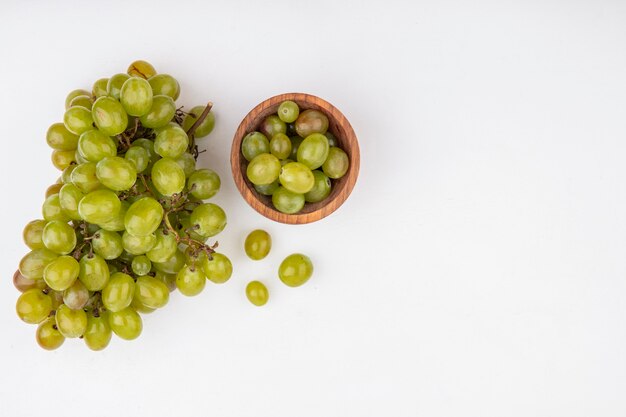 Top view of white grape berries in bowl and bunch of white grape on white background with copy space