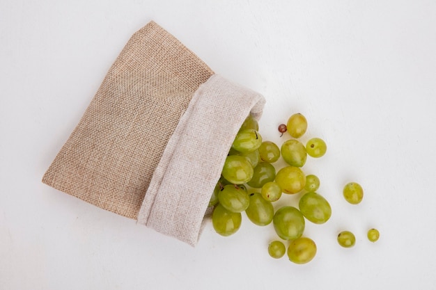 Top view of white grape berries spilling out of sack on white background