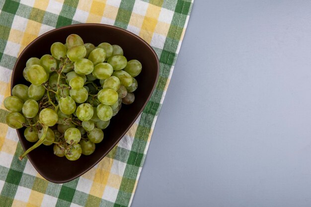 Top view of white grape in bowl on plaid cloth on gray background with copy space