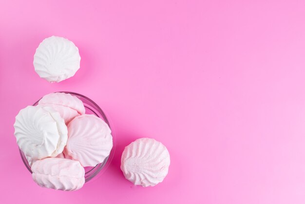A top view white meringues inside round glass bowl on pink