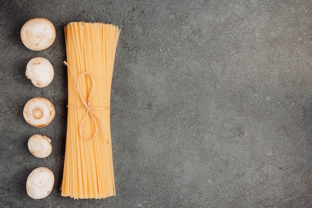 Top view white mushrooms and a bunch of spaghetti pasta on gray textured background. horizontal space for text