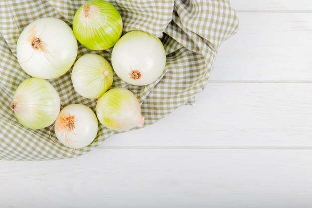 Top view of white onions on plaid cloth and wooden background with copy space