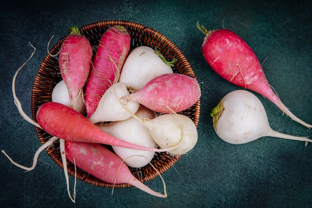 Top view of white and pinkish red root vegetable beetroots on a bucket on a green background
