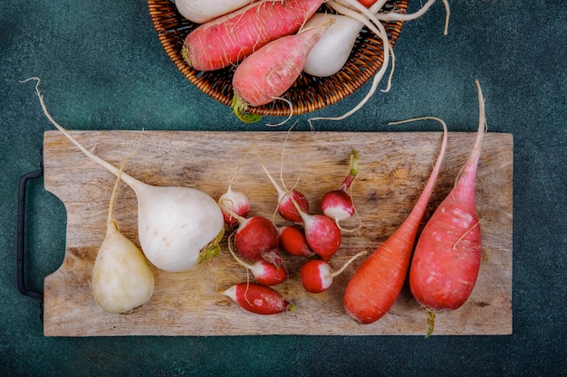 Top view of white and pinkish red root vegetable beetroots on a wooden kitchen board with radishes on a green surface