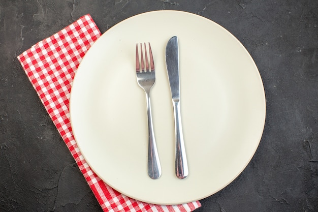 Вид сверху белая тарелка с вилкой и ножом на темной поверхности