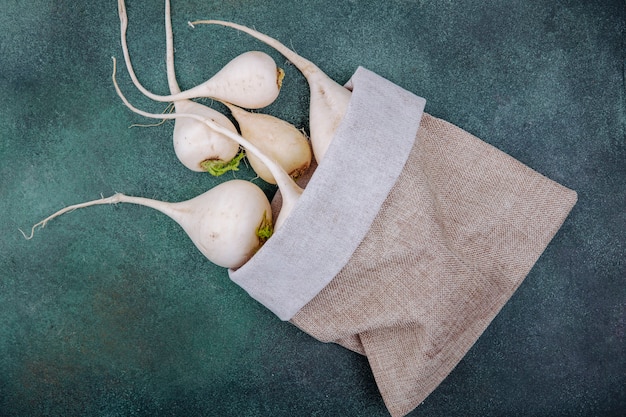 Top view of white root vegetable beetroots on a burlap bag on a green surface