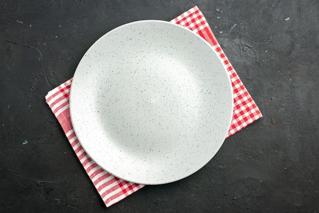 Вид сверху белая круглая тарелка на салфетке на темном столе
