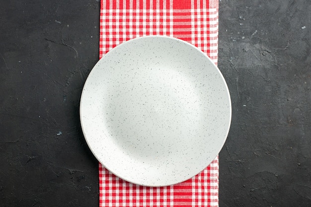 Top view white round plate on red and white checkered napkin on dark table copy place