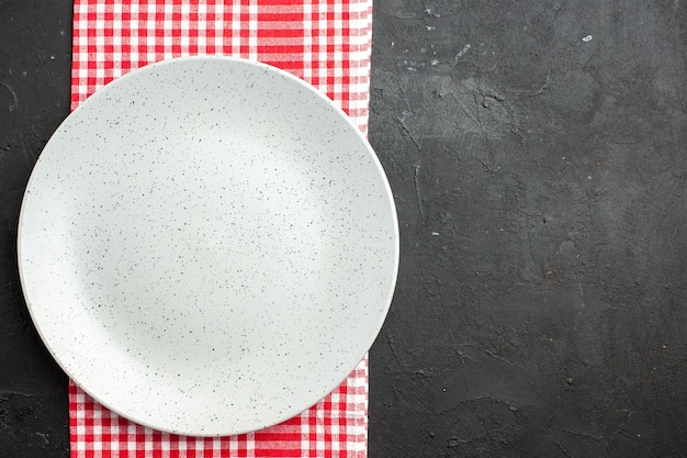 Free photo top view white round plate on red and white checkered napkin on dark table with copy place