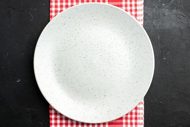 Top view white round plate on red and white checkered napkin on dark table