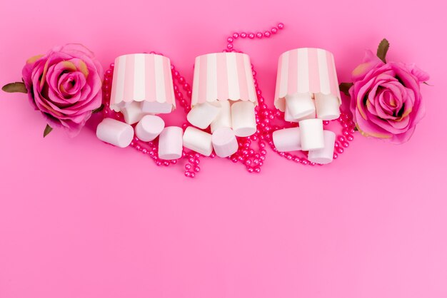 ピンクの机の上のピンクのバラ、ビスケットメレンゲ甘い紙パッケージ内の平面図白いおいしいマシュマロ
