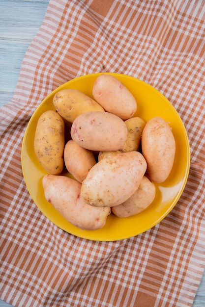 Top view of white and yellow potatoes in plate on plaid cloth and wooden surface