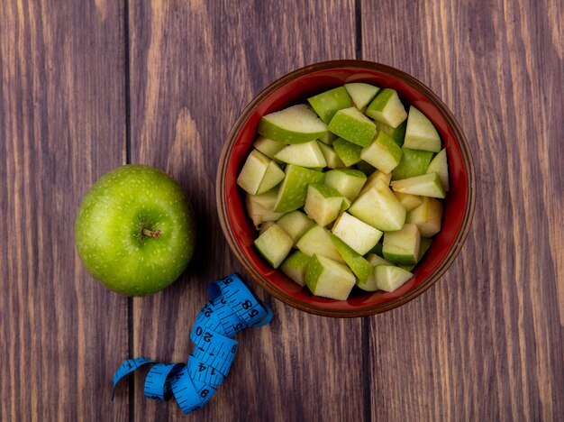 Top view of whole apple with chopped apple slices on a red bowl on a wooden surface