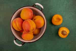 Free photo top view of whole apricots in bowl and half cut one on green background
