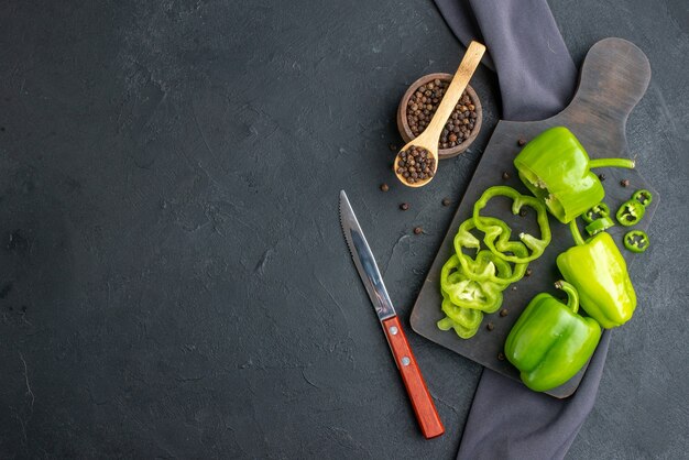 Top view of whole cut chopped green peppers on wooden cutting board on dark color surface