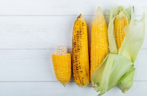 Top view of whole and cut corn cobs on wooden surface with copy space