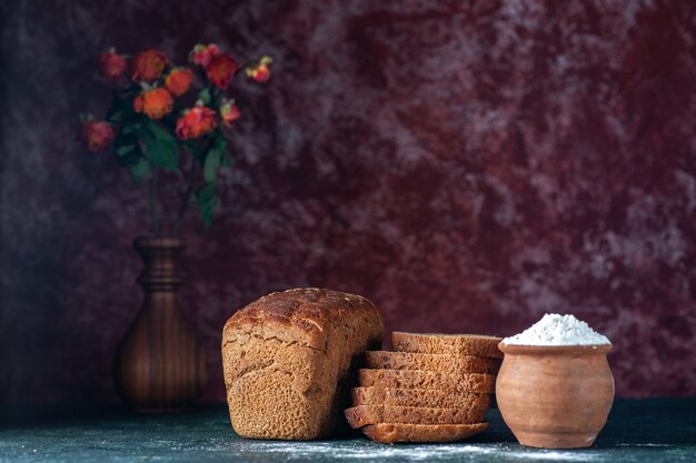 Top view of whole cut dietary black bread and flour in bowl flower pot on blue maroon colors background