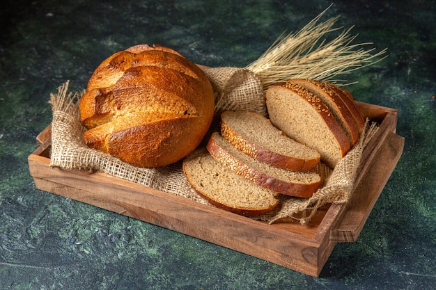 Free photo top view of whole and cut fresh black bread on towel in a brown wooden box on dark mix colors surface