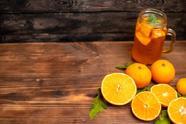 Top view of whole and cut fresh oranges with leaves and natural juice in a glass on the left side on a brown background