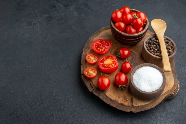 Top view of whole cut fresh tomatoes and spices on wooden board on the left side on black surface