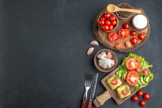 Top view of whole cut fresh vegetables and spices on wooden board white towel knife cheese on black surface