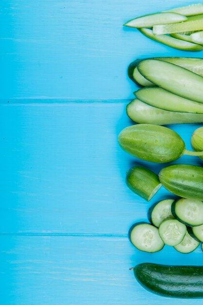 Top view of whole cut sliced cucumbers on right side and blue surface with copy space