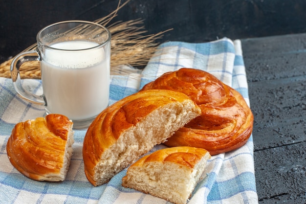 Вид сверху целой и нарезанной вкусной выпечки на синем полосатом полотенце и всплеск молока в стакане на синем