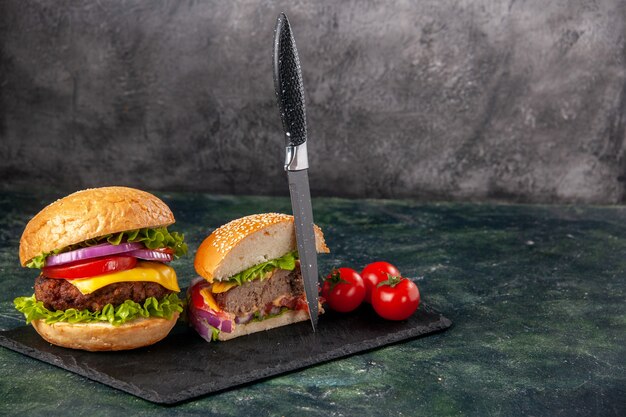 Вид сверху на целые нарезки различных вкусных бутербродов и помидоров с ножом для стеблей на черном подносе с правой стороны на поверхности темного цвета