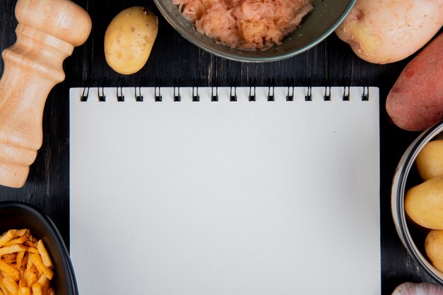 Top view of whole grated and fried potatoes around note pad with salt on wooden surface with copy space