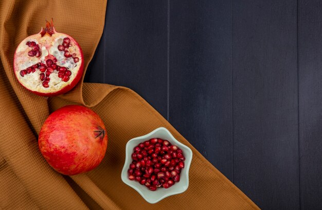 Top view whole half and peeled pomegranate on a brown towel on a black table