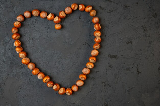 Top view of whole hazelnuts arranged in a heart shape on dark j