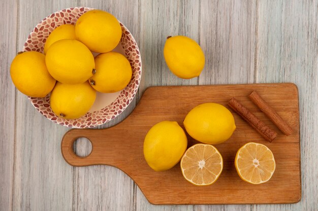 灰色の木製の壁にシナモンスティックと木製のキッチンボードに分離されたレモンとボウルにレモン全体の上面図