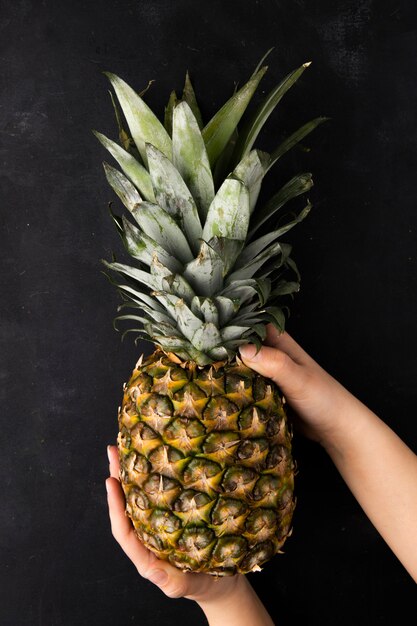 Top view of whole pineapple being held by woman hands on black surface