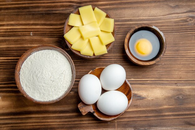 Вид сверху целые сырые яйца с мукой и сыром на коричневом столе, яйцо, тесто для завтрака, мучная пыль