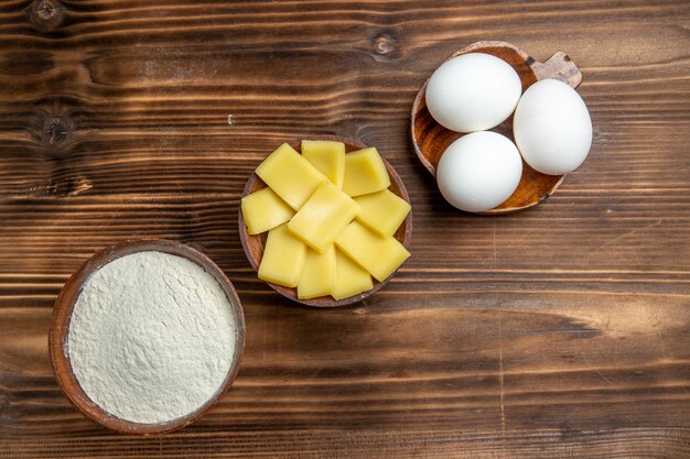 Top view whole raw eggs with flour and cheese on brown table eggs dough flour dust product