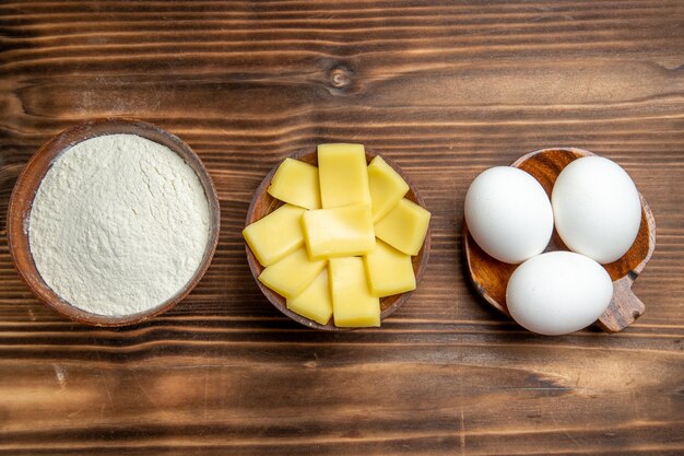 茶色のテーブルの卵生地小麦粉ダスト製品に小麦粉とチーズを入れた生卵全体の上面図