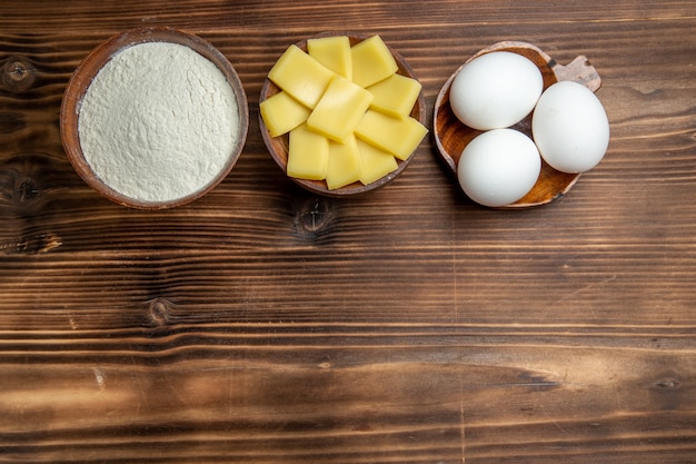 Top view whole raw eggs with flour and cheese on the brown table eggs dough flour dust products