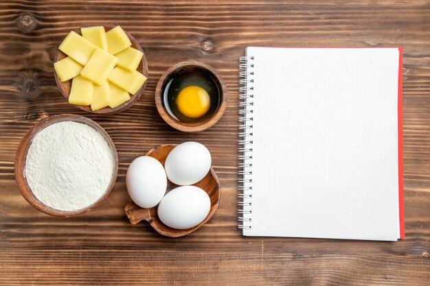 Top view whole raw eggs with flour and cheese on brown wooden table egg dough pastry flour dust