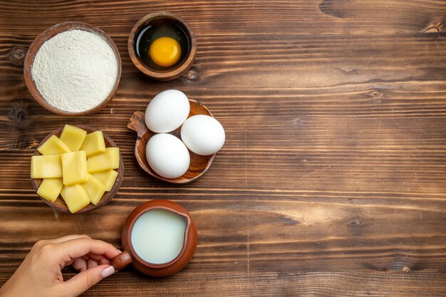 Top view whole raw eggs with flour milk and cheese on brown table egg dough flour dust products