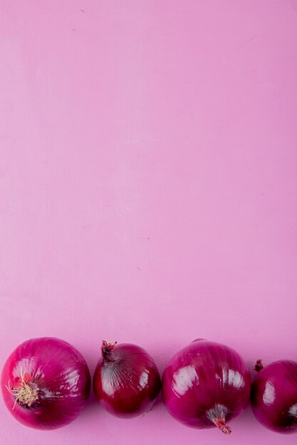 Top view of whole red onions on purple background with copy space