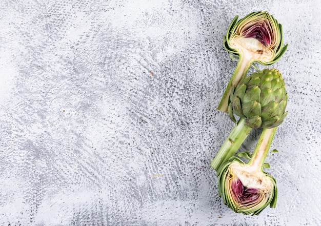 Free photo top view whole and sliced artichokes on light gray background. horizontal space for text