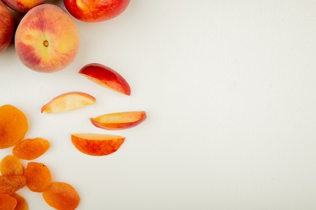 Free photo top view of whole and sliced peaches and yellow raisins on left side and white surface with copy space