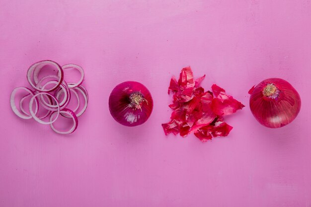 Top view of whole and sliced red onion with skin on purple background with copy space