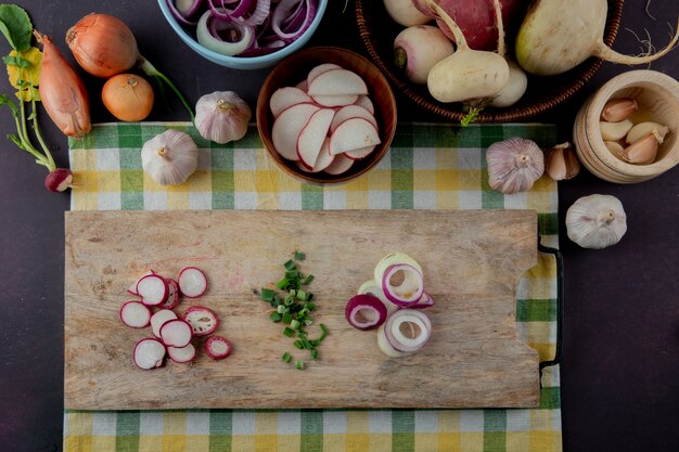 Top view of whole and sliced vegetables as shallot garlic radish scallion onion on maroon background