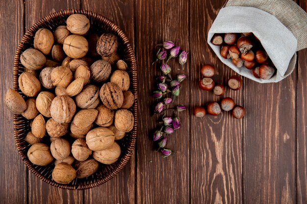 Top view of whole walnuts in a wicker basket and hazelnuts scattered from a sack on wooden background
