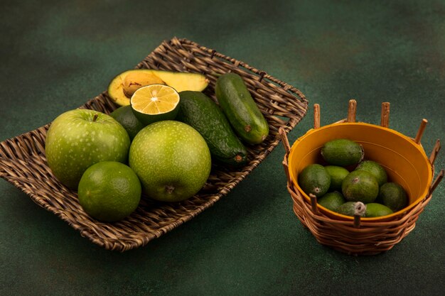 녹색 표면에 양동이에 feijoas와 녹색 사과 라임 아보카도와 오이와 같은 건강 식품의 고리 버들 트레이의 상위 뷰